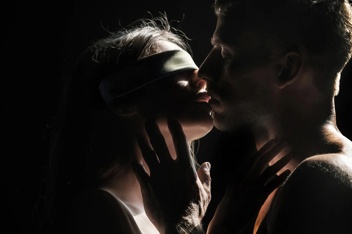 A blindfolded woman and a man about to kiss, symbolizing trust, control, and the sensual tension behind cuckold fantasies.